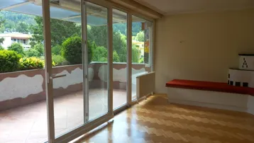 Helles Wohnzimmer mit Parkettboden, Kachelofen und Zugang zu einer großen Terrasse mit Bergblick.