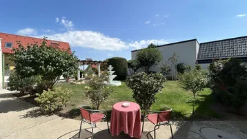 Gemütlicher Gartenbereich mit Sitzgelegenheiten und einem dekorativen Brunnen unter blauem Himmel.