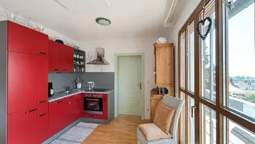 Funktionale Küche mit roten Schränken, integriertem Backofen und hellem Holzboden.