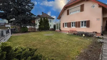 Hausfassade mit großem Gartenbereich und gepflegtem Rasen unter blauem Himmel.