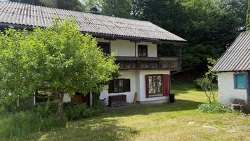 Traditionelles Landhaus mit Holzbalkon und Satteldach, umgeben von grüner Natur.