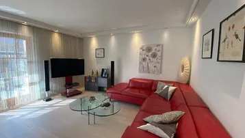 Helles Wohnzimmer mit rotem Ecksofa, Parkettboden und Zugang zum Balkon.