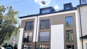 Modernes Mehrfamilienhaus mit großen Fenstern, französischen Balkonen und Dachgauben in städtischer Umgebung.