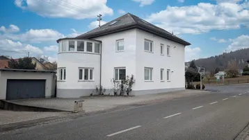 Weißes Wohnhaus mit markantem Rundbau und separater Garage an der Straße.