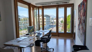 Helles Büro mit großen Fenstern, Holzboden und einem weiten Blick auf die Stadt und Berge.