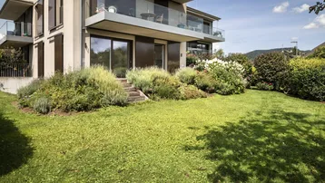 Modernes Gebäude mit mehreren Balkonen und einem gepflegten Gartenbereich mit Rasenfläche.