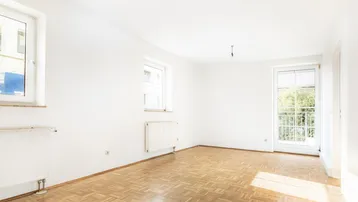 Helles, unmöbliertes Zimmer mit Parkettboden, großen Fenstern und Zugang zu einem französischen Balkon.