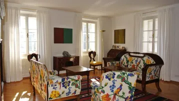 Helles Wohnzimmer mit farbenfrohen Sofas, Parkettboden und klassischen Holzmöbeln, durchflutet von natürlichem Licht.