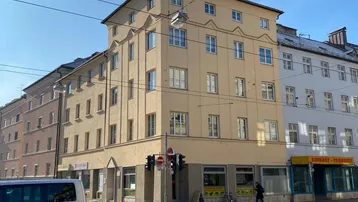 Mehrstöckiges Gebäude an einer belebten Straßenecke mit Geschäften im Erdgeschoss und Wohnungen darüber.