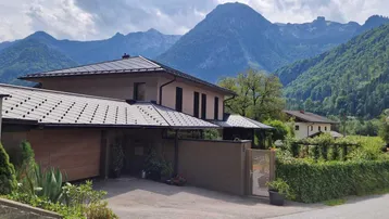 Modernes Haus mit dunklem Dach und gepflegtem Vorgarten vor einer beeindruckenden Bergkulisse.