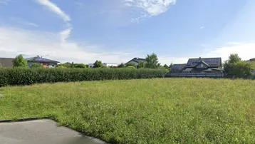 Weitläufiges, unbebautes Grundstück mit grüner Wiese und Hecken, umgeben von Wohnhäusern.