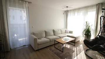 Helles Wohnzimmer mit beigem Ecksofa, Holzboden und einem Hängesessel am Fenster.