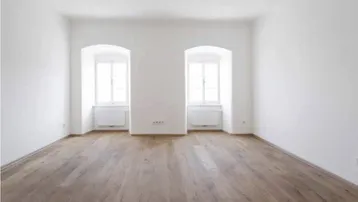 Helles, leeres Zimmer mit Holzboden und zwei Rundbogenfenstern, bereit zur Einrichtung.