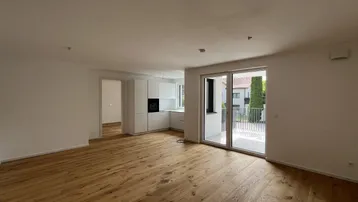 Heller offener Wohnbereich mit Holzboden, integrierter Küche und Zugang zu einem Außenbereich.