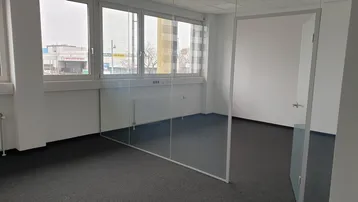 Helles Büro mit Teppichboden und großen Fenstern, die einen Blick auf die Umgebung bieten.