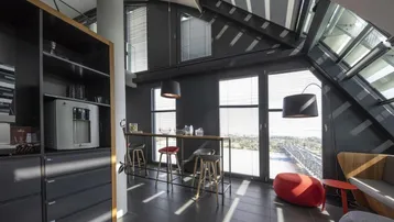 Moderner Pausenbereich mit Bar, dunklen Fliesen und großer Fensterfront, die einen weiten Blick bietet.