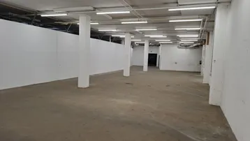 Großer, leerer Raum mit Betonboden und weißen Wänden, beleuchtet von zahlreichen Deckenleuchten.