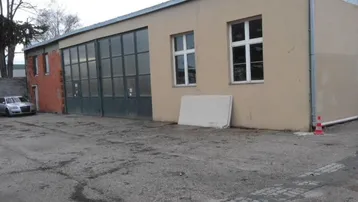 Gebäudeansicht einer Gewerbehalle mit großen Toren und Fenstern sowie einem gepflasterten Vorplatz.
