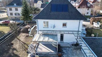 Luftaufnahme des Hauses mit Dach, Solarpaneelen, Terrasse und Gartenbereich in einer Wohngegend.