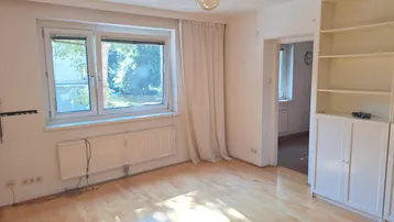 Helles Wohnzimmer mit Parkettboden, großem Fenster und Blick ins Grüne.