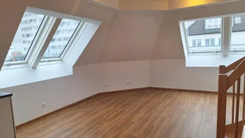 Heller Wohnraum im Dachgeschoss mit Laminatboden, weißen Wänden und mehreren Dachfenstern.