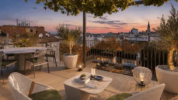 Geräumige Dachterrasse mit gemütlichen Sitzbereichen, Pflanzen und Stadtblick bei Sonnenuntergang.