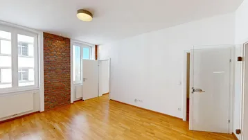 Helles Zimmer mit Holzboden, einer Akzentwand aus Ziegeln und großen Fenstern.