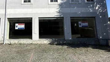 Fassade eines Geschäftsgebäudes mit großen Schaufenstern und Kopfsteinpflaster davor unter blauem Himmel.