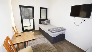 Helles Schlafzimmer mit Einzelbett, kleinem Tisch und Zugang zu einem Balkon.