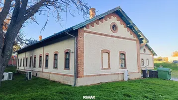 Altes Gebäude mit Ziegel- und Putzfassade, umgeben von Gras und Bäumen unter blauem Himmel.