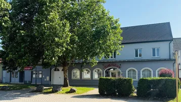 Ansicht des Gebäudes von außen mit einem großen Baum und einem Café-Restaurant im Erdgeschoss.