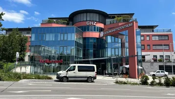 Modernes Gesundheitszentrum mit Glasfassade und mehreren Etagen unter blauem Himmel.