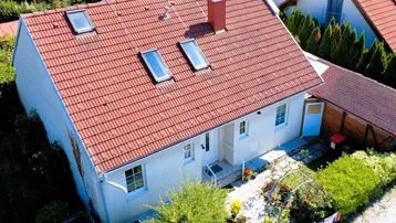Luftaufnahme eines Einfamilienhauses mit rotem Ziegeldach und Dachfenstern, umgeben von viel Grün.