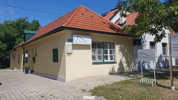 Gelbes Gebäude mit rotem Ziegeldach und grünen Fensterläden unter blauem Himmel.