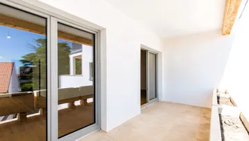 Geräumiger Balkon mit Fliesenboden und Schiebetüren, bietet Blick auf die umliegenden Dächer.