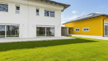 Außenansicht eines modernen Hauses mit weißer Fassade, großem Garten und angrenzendem gelbem Gebäude.