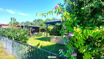Gepflegter Gartenbereich mit Rasenfläche, Zaun und einer überdachten Sitzecke im Freien.