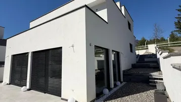 Seitliche Ansicht der modernen Villa mit Garagentoren und gepflastertem Zugangsbereich.