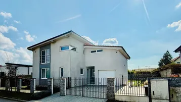 Modernes Einfamilienhaus mit gepflegtem Vorgarten, Einfahrt und sonnigem Himmel.