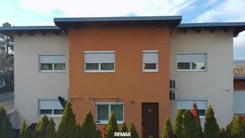 Vorderansicht des modernen Hauses mit beiger und oranger Fassade sowie mehreren Fenstern mit Rollläden.