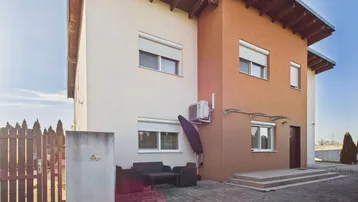 Seitliche Ansicht des Hauses mit einer kleinen gepflasterten Terrasse und Außenmöbeln unter einem Vordach.