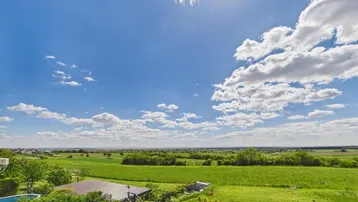 Weitläufiger Blick über grüne Felder und die Landschaft unter einem strahlend blauen Himmel.