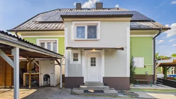 Vorderansicht des Hauses mit Solarpaneelen auf dem Dach und einem Carport im Eingangsbereich.