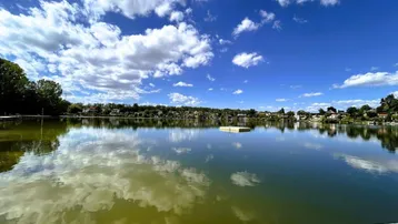 Malerischer See mit Holzanleger und Häusern am Ufer unter einem bewölkten Himmel.