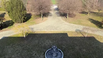Panoramablick von oben auf den Garten mit Brunnen und die weite, grüne Landschaft im Hintergrund.