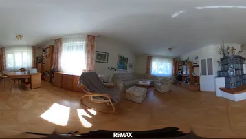 Gemütliches Wohnzimmer mit traditionellem Kachelofen, Holzmöbeln und viel Tageslicht durch die Fenster.