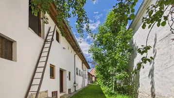 Langes, weißes Gebäude mit Leiter und grünem Grasweg unter blauem Himmel.