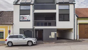 Moderne Fassade eines Neubaus mit Balkonen, großen Fenstern und Tiefgaragenzufahrt.