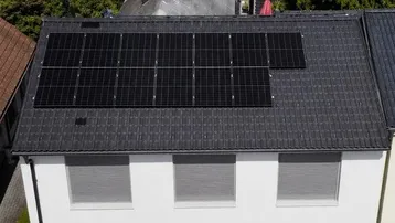 Luftaufnahme eines modernen Einfamilienhauses mit Photovoltaikanlage auf dem Dach und gepflegter Umgebung.