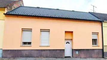 Einfaches Einfamilienhaus mit pastellfarbener Fassade und Rollläden an den Fenstern.